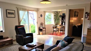 A living room with a sofa, armchair, and coffee table. There is a dining area with a table and chairs. A plant is visible in the corner.