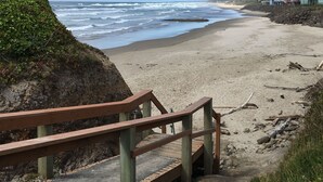 A wooden staircase leading down to a sandy beach with ocean waves in the background.