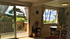 A room with a sliding glass door leading to a balcony, a dining area with a table and chairs, and a view of the ocean.