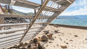 A beach with a metal structure, a rocky shoreline, and a view of mountains in the distance. - Grandview 627 Waterfront condo on Lake Chelan (Chelan)