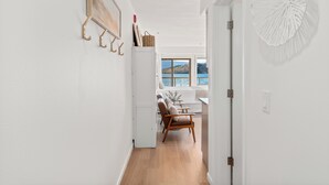 Un couloir doté d’un plancher en bois, de murs blancs et d’une porte donnant sur une pièce avec vue sur la mer.