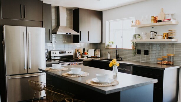 A modern kitchen with a central island, stainless steel appliances, and a backsplash of gray tiles. - The Phx Bungalow located in north-central phoenix. (Phoenix)
