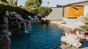 A swimming pool with a waterfall feature, surrounded by rocks and a wooden fence. - The Phx Bungalow located in north-central phoenix. (Phoenix)