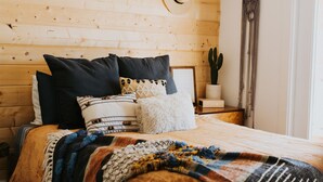 A bedroom with a wooden headboard, a ceiling fan, a bed with multiple pillows and a blanket, a cactus plant, and a door with a curtain. - The Phx Bungalow located in north-central phoenix. (Phoenix)