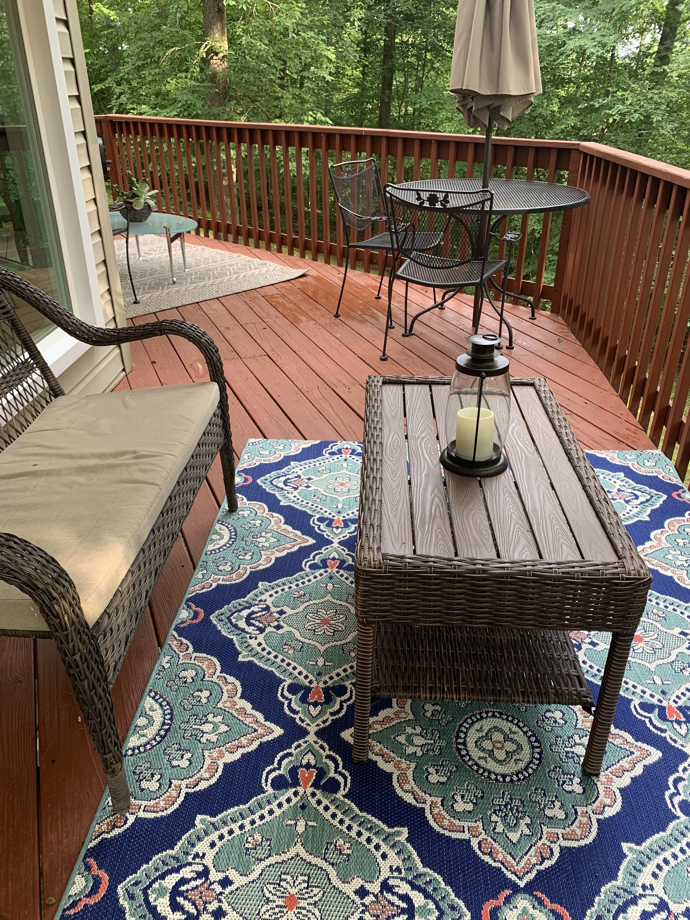 Una terraza de madera con mobiliario de mimbre, un tapiz estampado y una mesa con una vela.