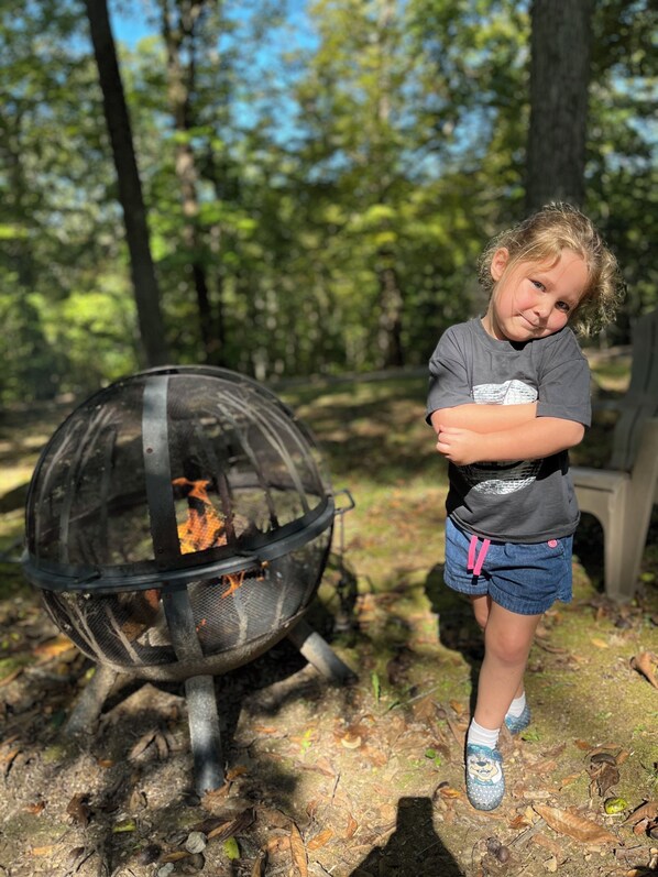 A child standing next to a fire pit in a wooded area.