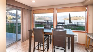 Un espace repas comprenant une table et des chaises, de grandes fenêtres offrant une vue sur un lac et des montagnes, et une porte-fenêtre coulissante donnant sur une terrasse extérieure.