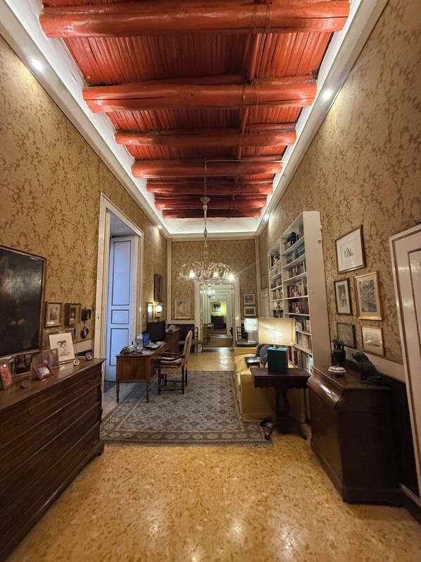 A room with a wooden ceiling, a chandelier, a desk, a bookshelf, and a door.