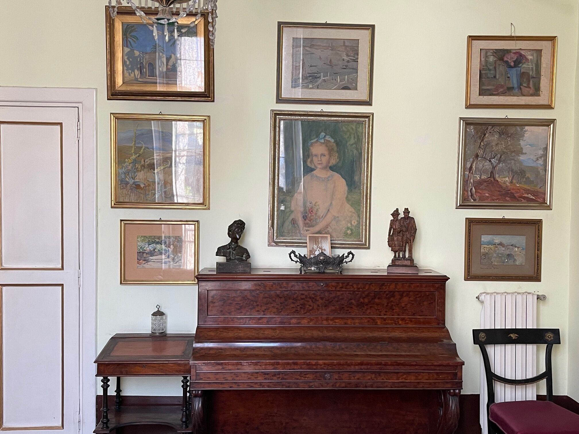 Una habitación con un piano de madera, una silla y varias obras de arte enmarcadas en la pared.
