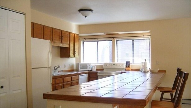 A kitchen with wooden cabinets, a white refrigerator, a microwave, a stove, and a large island with two wooden chairs. - Luxury and location, King & Queen pillow, fireplace, whirlpool tub (Frisco)