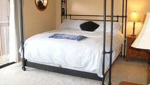 A four-poster bed with white bedding, a round mirror on the wall, and a bedside table with a lamp. - Luxury and location, King & Queen pillow, fireplace, whirlpool tub (Frisco)