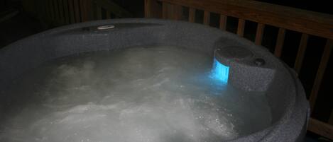 Un jacuzzi con burbujas visibles, una terraza de madera y una barandilla.