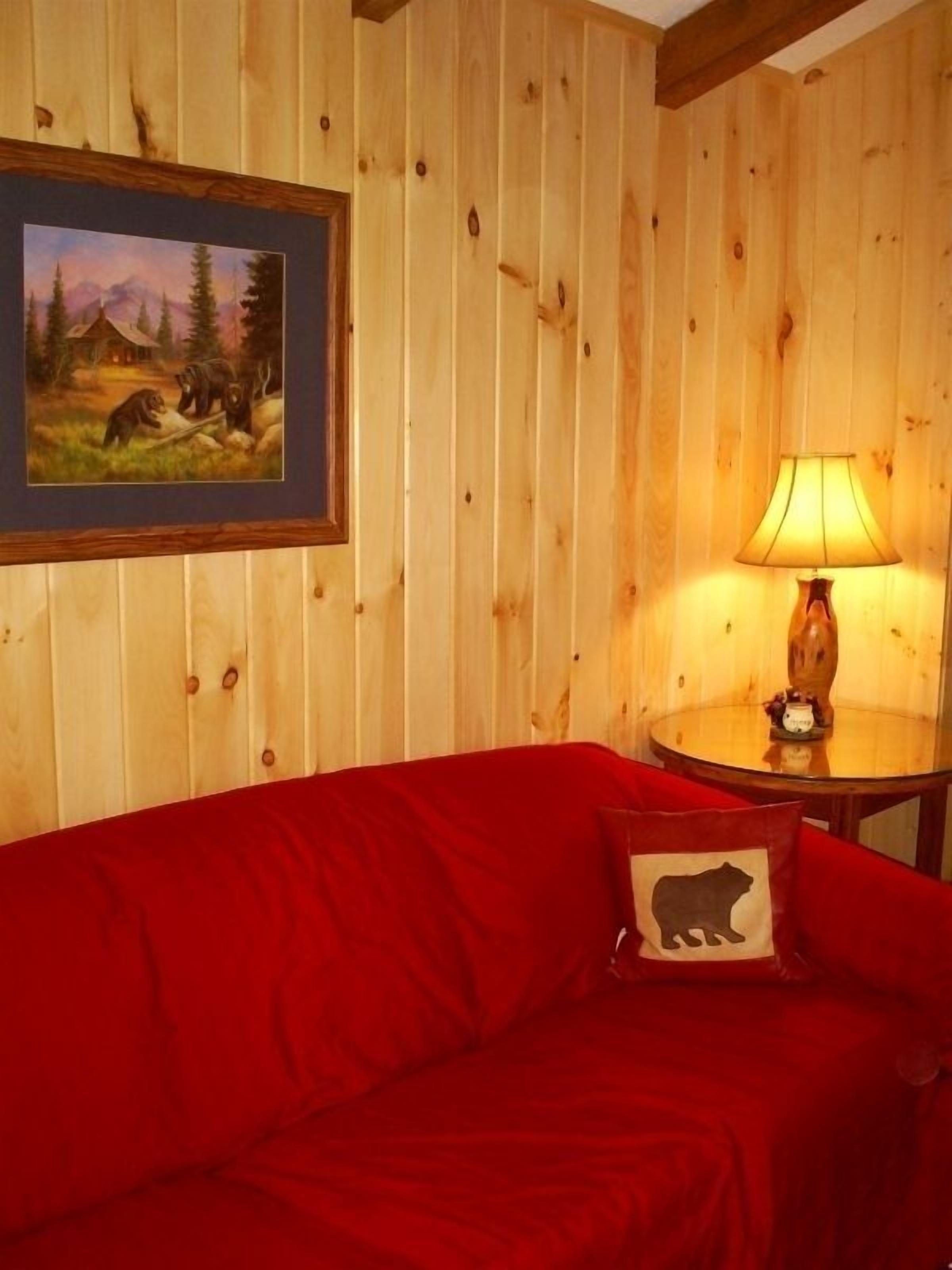A wooden-paneled room with a red sofa, a lamp, and a framed picture of a bear.