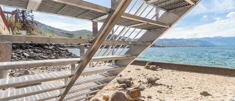 A beach with a metal structure, a rocky shoreline, and a view of mountains in the distance.