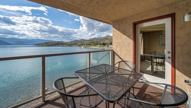 Un balcon avec une table et des chaises donnant sur une étendue d’eau et sur des montagnes lointaines.