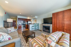 Een woonkamer met een bank, fauteuil en salontafel, een keuken met inbouwapparatuur, en een open haard.