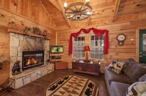 A cozy log cabin interior with a stone fireplace, wooden walls, a television, and a green door. - Cozy 2 BR w/Hot Tub, Pool Table, Wi-Fi, Close to Gatlinburg (Sevierville)