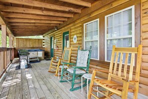 A wooden cabin with a porch, rocking chairs, a grill, and a small table.