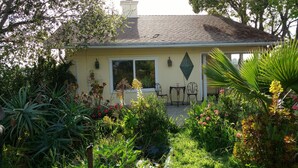 Una casa con jardín delantero, un patio con sillas y una ventana con vista al jardín.