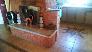 Cozy kitchen with a brick fireplace, modern gas stove, and traditional wood-burning stove, complete with a mantel featuring decorative items.