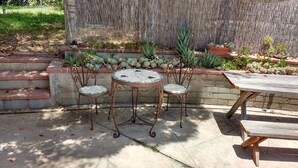 Un patio con una mesa redonda y dos sillas, un banco de madera y un muro decorativo con plantas.