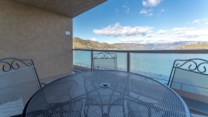 En balkon med et rundt metalbord og stole, med udsigt over en sø og bjerge i baggrunden.