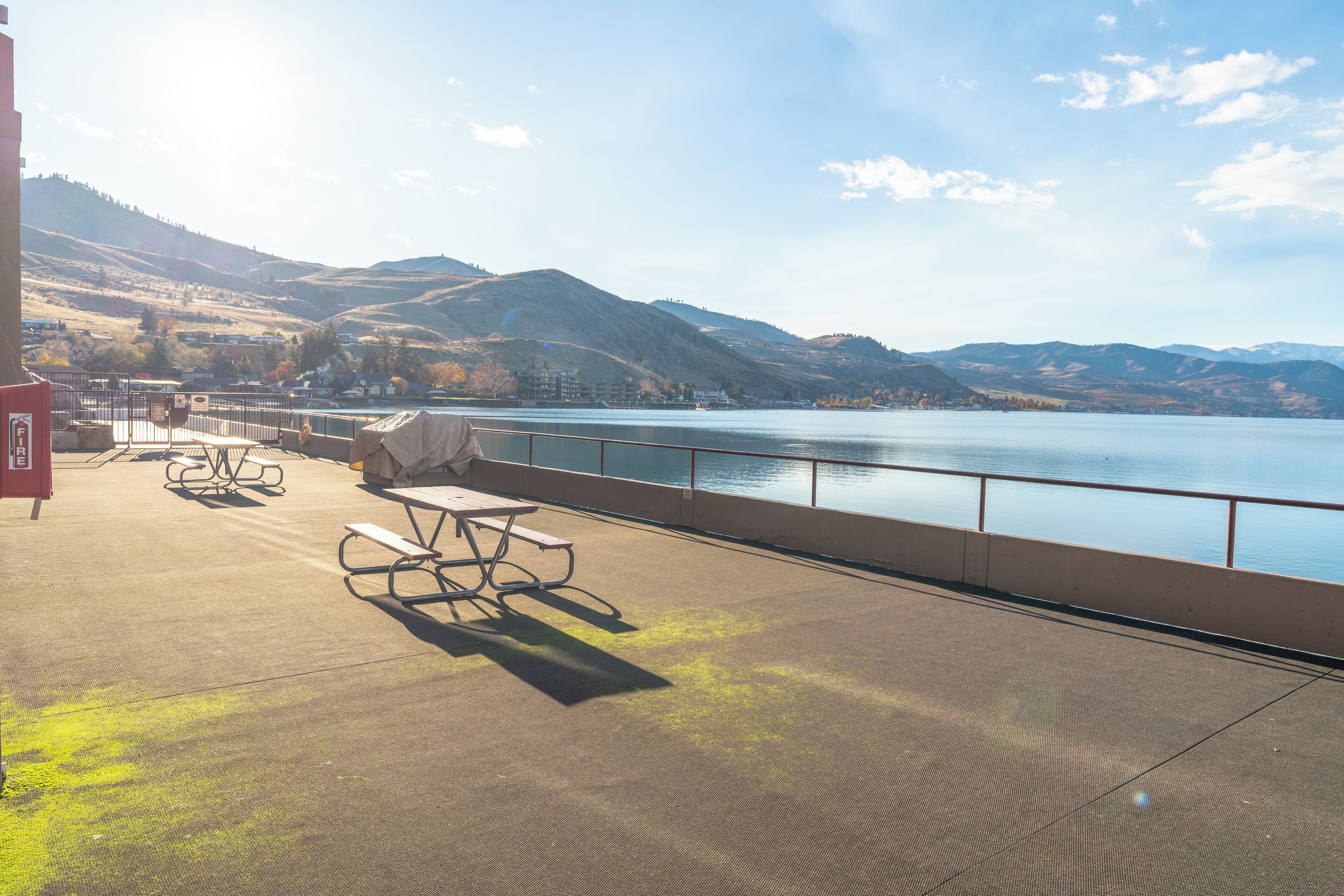 Terraço com mesas de piquenique e vista para um lago e montanhas.