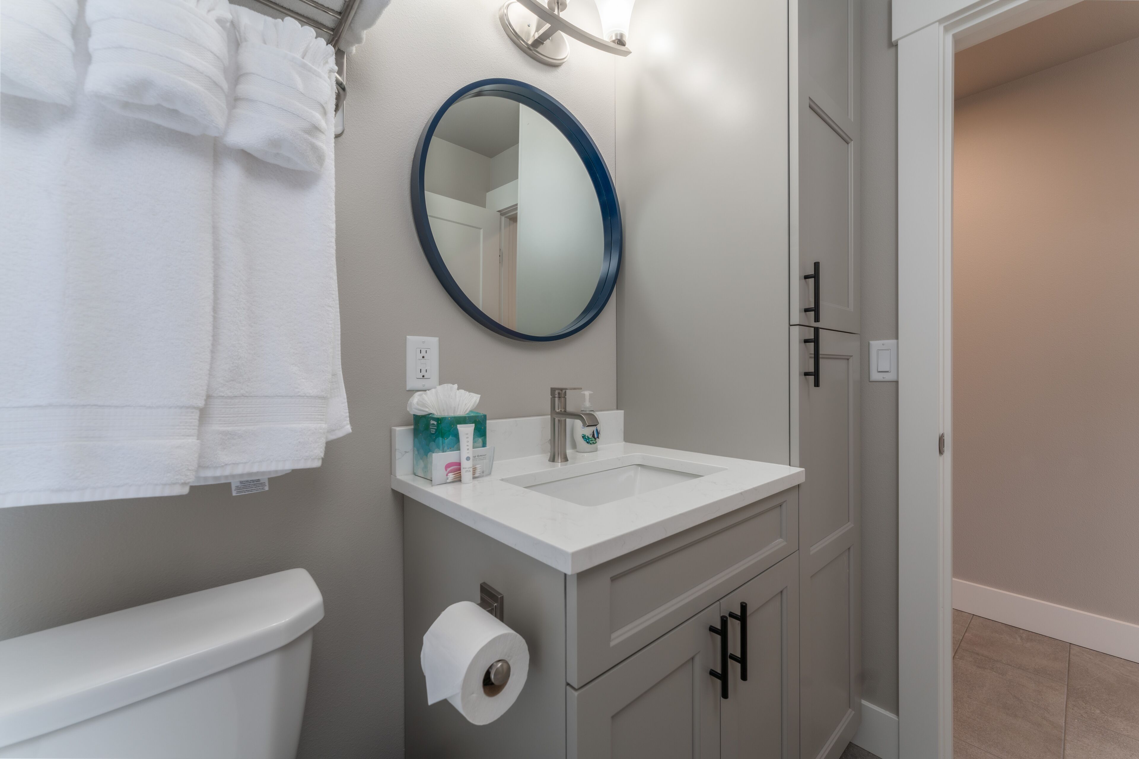 Une salle de bain avec un lavabo blanc, un miroir rond et des toilettes.