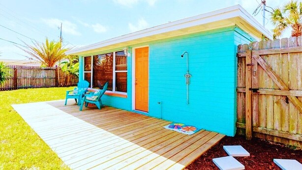 A small, single-story house with a blue exterior, a wooden deck, and a small patio area with two blue chairs. - Super Cute Beach Home *Recommended** Casa Azalea (Ormond Beach)