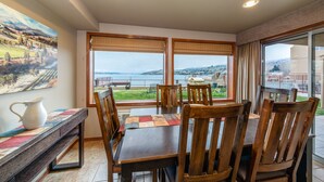 A dining area with a table and chairs, a pitcher, and a view of a landscape through large windows. - GrandView #102, 2-Bedroom Waterfront Condo (Chelan)