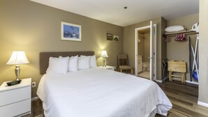 Een hotelkamer met een groot bed, twee bedlampen, een nachtkastje, een stoel, een kledingkast en een badkamer die door een geopende deur zichtbaar is.
