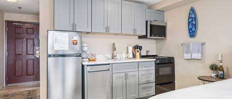A modern kitchen with grey cabinets, a stainless steel refrigerator, a microwave, and a stove. There is a small table with a plant and a bottle on it.