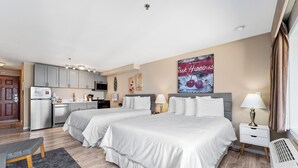 Hotellihuone, jossa on kaksi sänkyä, pieni keittiö, ruokailutila ja kylpyhuone.