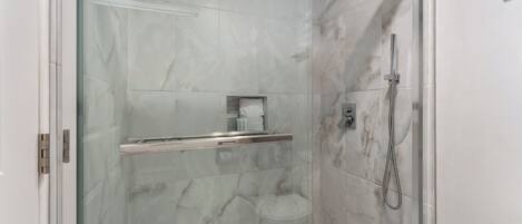 Una ducha moderna con mampara de vidrio, cabezal de ducha manual y grifo monomando.