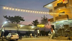 Un espace extérieur abrité où se trouvent une voiture et une moto, un bâtiment doté d’un balcon et des guirlandes lumineuses suspendues au-dessus.