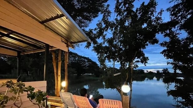Un espace extérieur aménagé avec des chaises et une table, offrant une vue sur une étendue d’eau paisible et des arbres.