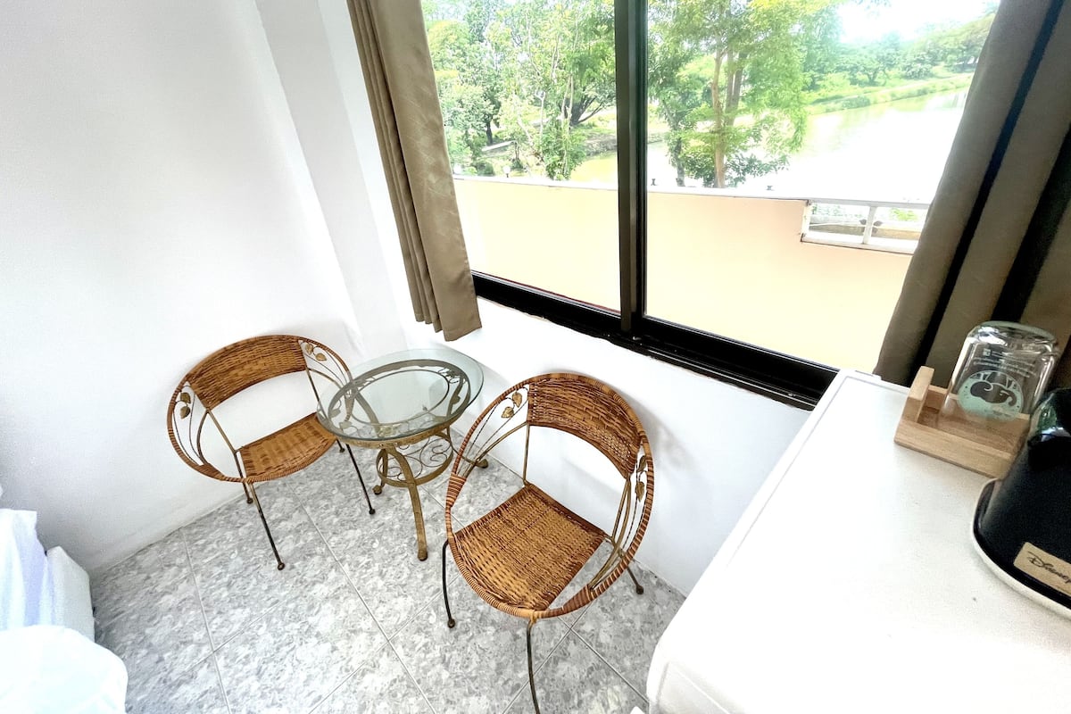 Un balcón con una mesa de vidrio y sillas de mimbre, con vistas a un paisaje verde.