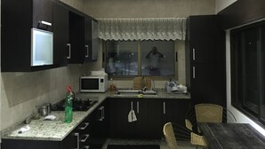 Une cuisine de taille réduite, dotée de meubles de rangement sombres, d’un four à micro-ondes, d’un évier et d’une fenêtre donnant sur la rue.