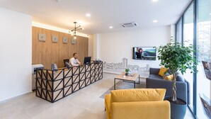 A modern reception area with a wooden reception desk, a large window with a cityscape view, and a seating area with a sofa and a coffee table. - City Inn (Pristina)