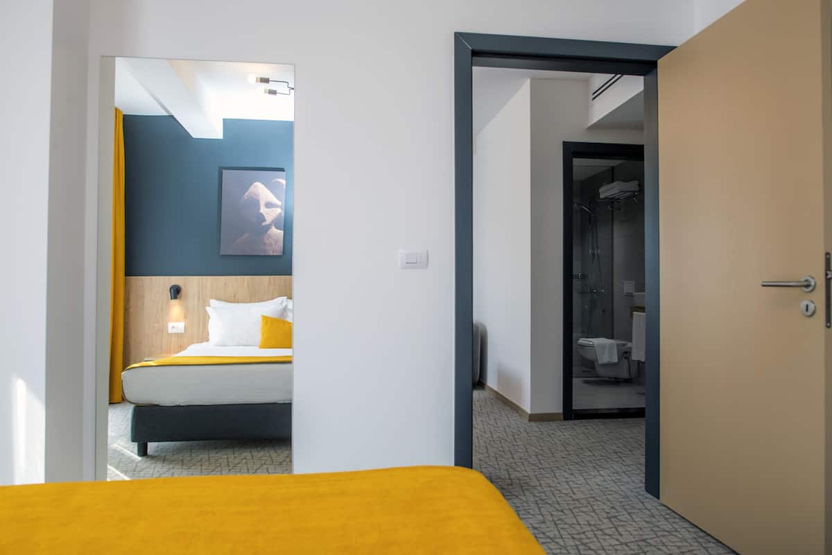 A hotel room with a bed, a bathroom with a shower, and a hallway.