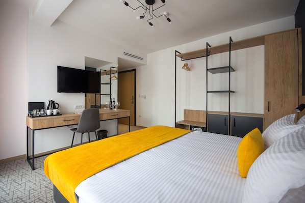 A modern hotel room with a bed, a desk, a chair, a TV, and a wardrobe.