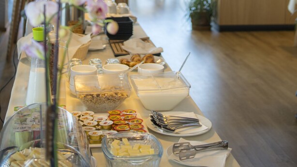 A buffet setup with various food items and utensils. - City Inn (Pristina)