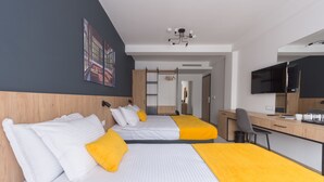 A hotel room with two beds, a desk, a chair, a TV, and a door leading to another room. - City Inn (Pristina)