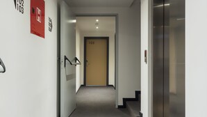 A modern hallway with a carpeted floor, a fire alarm on the left, and an elevator on the right. - City Inn (Pristina)