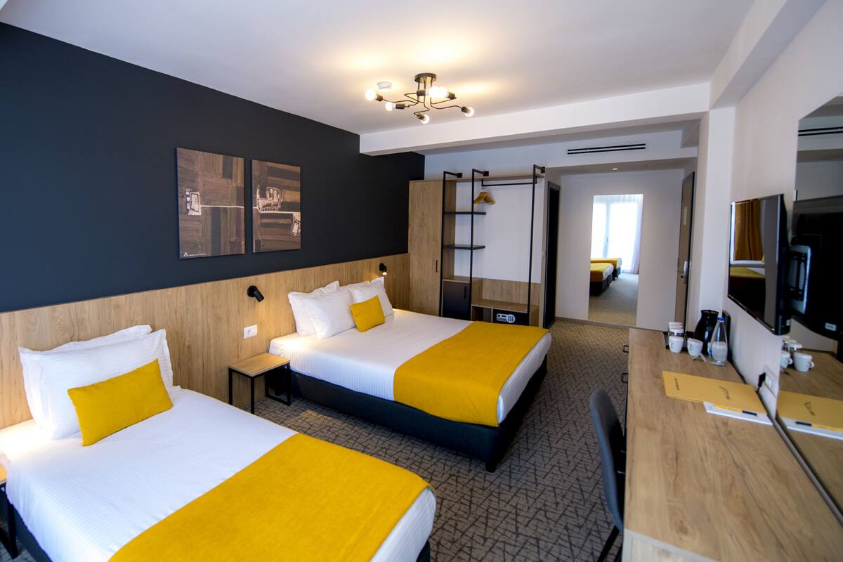 A hotel room with two beds, a desk, a TV, and a bathroom visible through an open door.