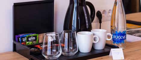 A tray with a coffee maker, two glasses, a mug, a bottle of water, and tea packets.
