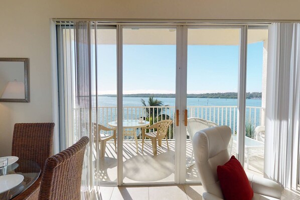 A balcony with a table and chairs, a wicker chair, and a white armchair with a red pillow.