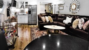 A modern living room with a black marble coffee table, a brown leather sofa with patterned cushions, and a large mirror on the wall.