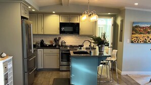 A modern kitchen with a central island, stainless steel appliances, and a dining area with a white sofa. - New Home w Expansive Ocean and Sunset Views, Steps to the Seal Cove Beach (Moss Beach)