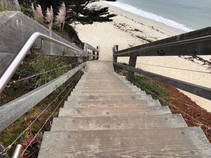 A wooden staircase leading to a beach with a railing on both sides.